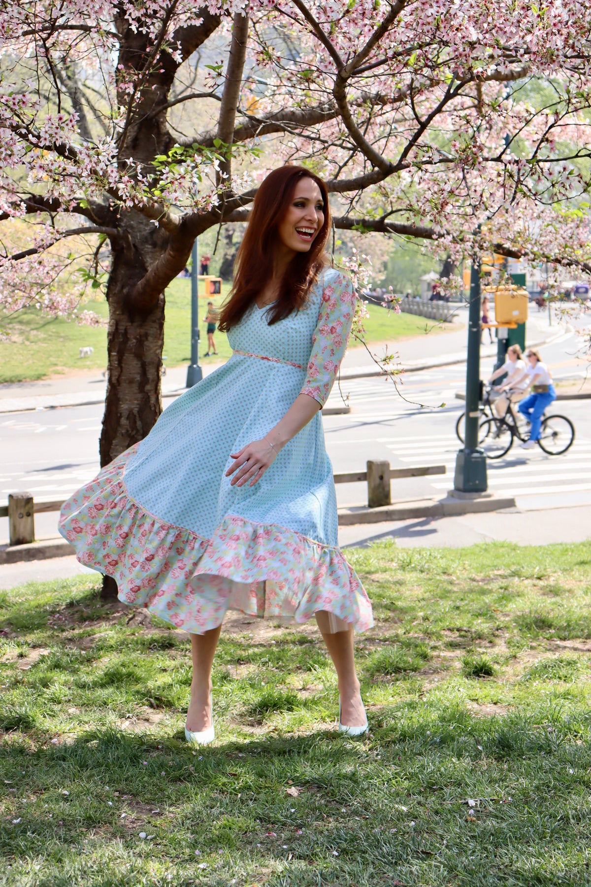 Model in aqua blue print midi dress with sleeves and lower ruffle in print and blue rose print swirling her skirt.t