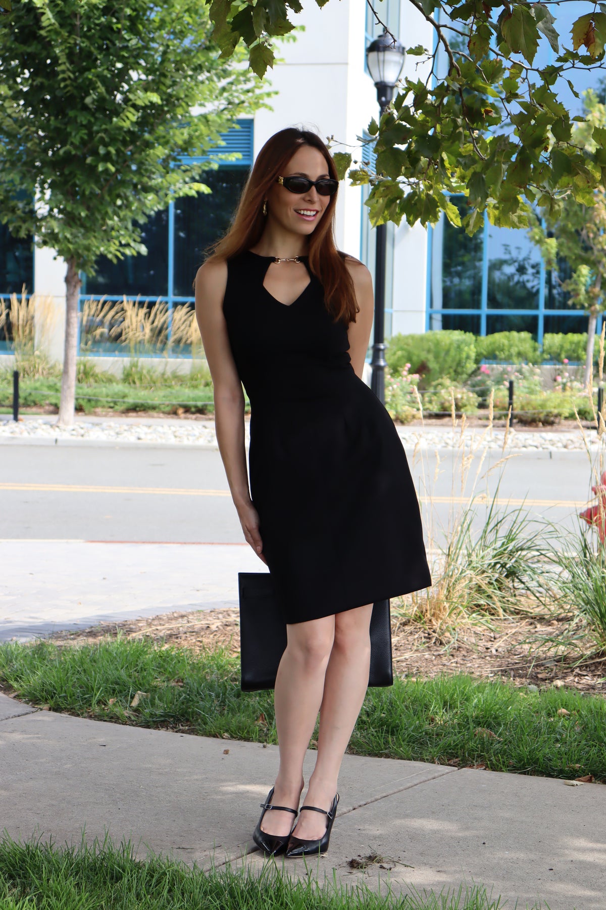 Model wearing our Black Snaffle Bit Keyhole Ponte Dress, posing in the shade with sunglasses and classic black bag and heels