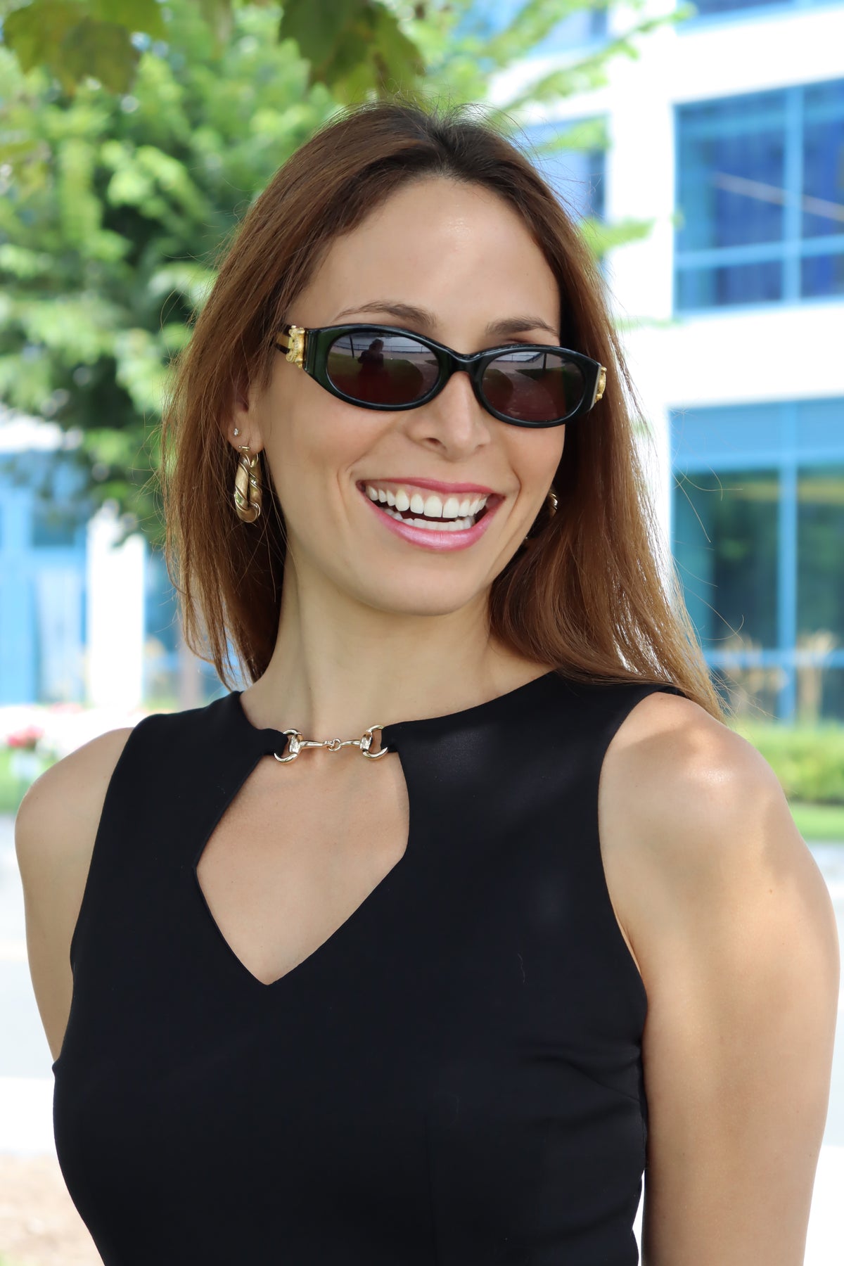 Close up of our Model wearing our Black Snaffle Bit Keyhole Ponte Dress, with a detailed view of snaffle bit and keyhole cut out, smiling in the shade sporting sunglasses and gold hoops complimenting the gold snaffle bit on the dress