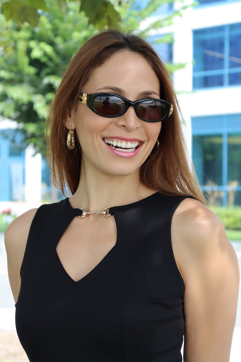Close up of our Model wearing our Black Snaffle Bit Keyhole Ponte Dress, with a detailed view of snaffle bit and keyhole cut out, smiling in the shade sporting sunglasses and gold hoops complimenting the gold snaffle bit on the dress