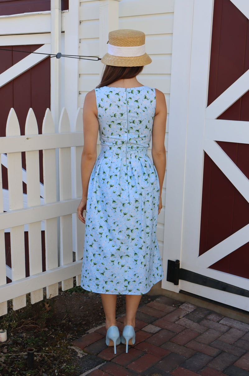 Back of Model wearing a midi light blue dress with peek-a-boo bow front, in front of a barn.