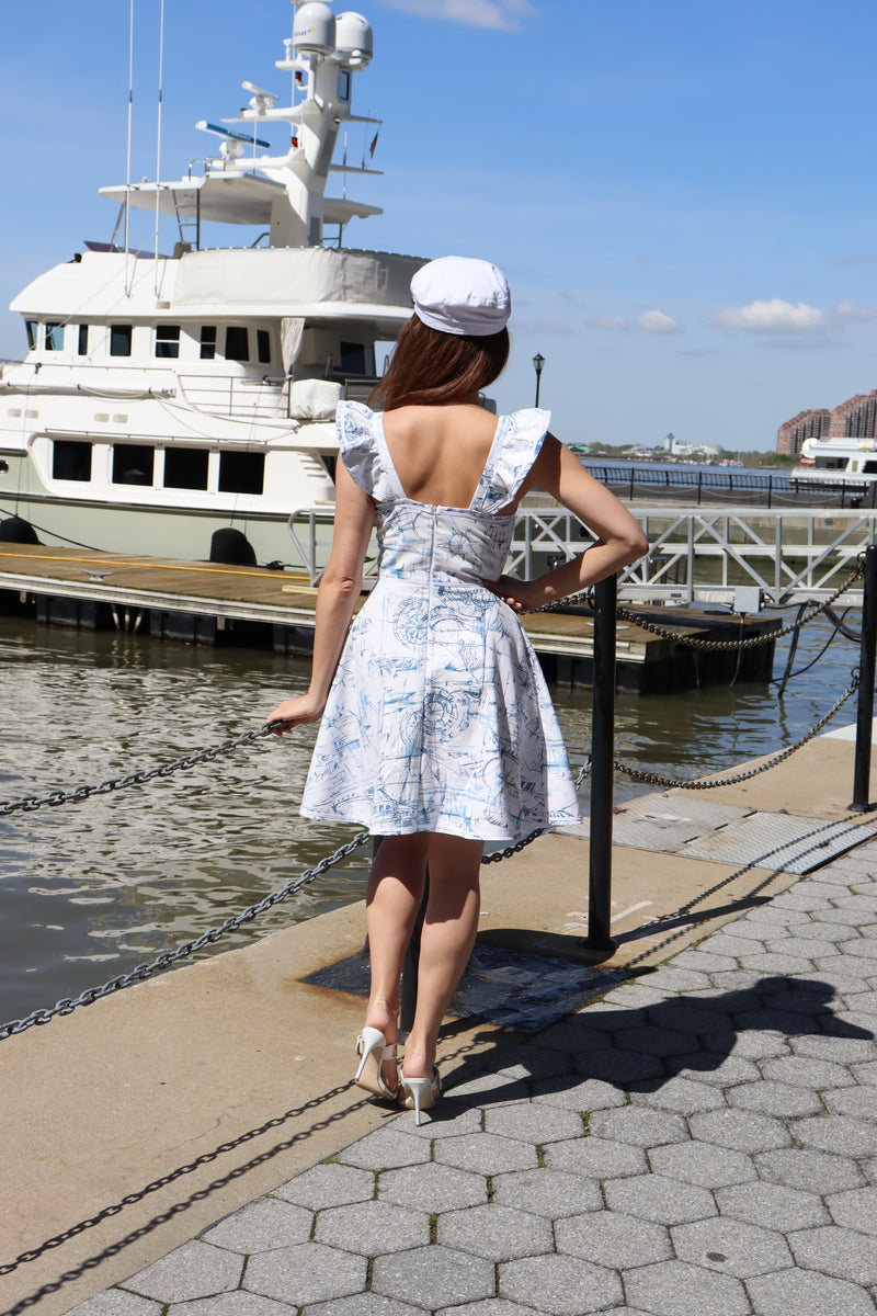 Back of model wearing heavy toile schooner print and a white hat standing in front of a boat.
