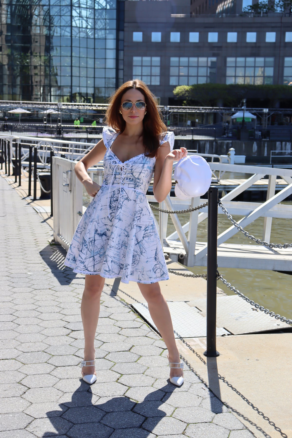 Model wearing heavy toile schooner print with one hand on her hip holding a white hat.