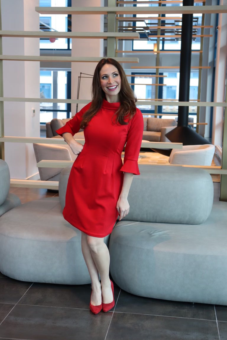 Model wearing a red dress with 3/4 sleeves with a hand on her hip, smiling.