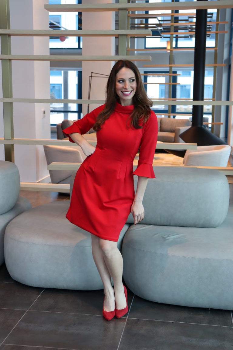 Model wearing a red dress with 3/4 sleeves with hand on her hip, smiling.