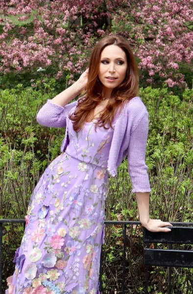 Model leaning on railing in lilac cropped sweater with matching lilac appliquéd floral dress.