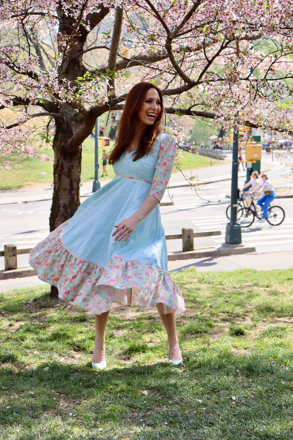 Model in aqua blue print midi dress with sleeves and lower ruffle in print and blue rose print swirling her skirt.t 
