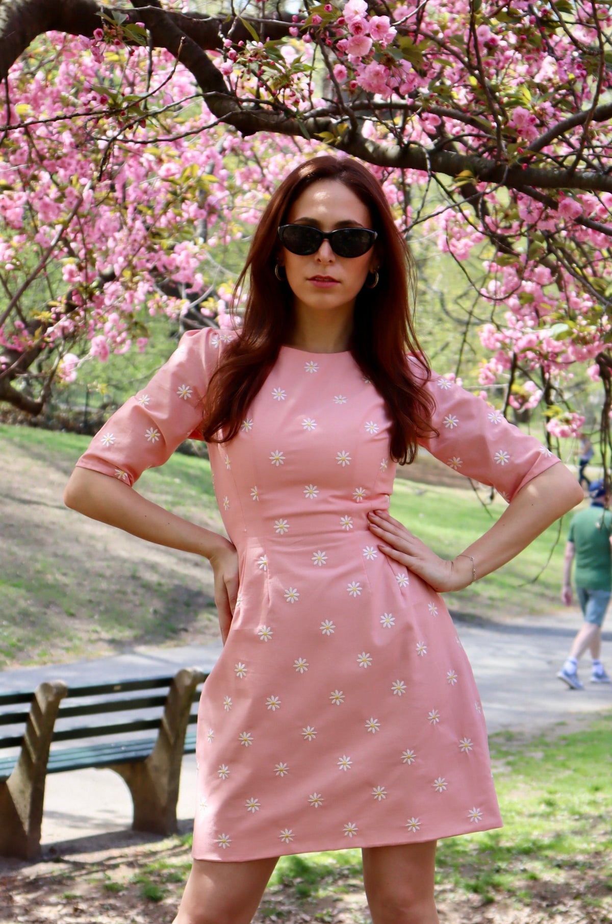 Model in peachy pink short dress with white daisy appliques in front of a cherry tree.