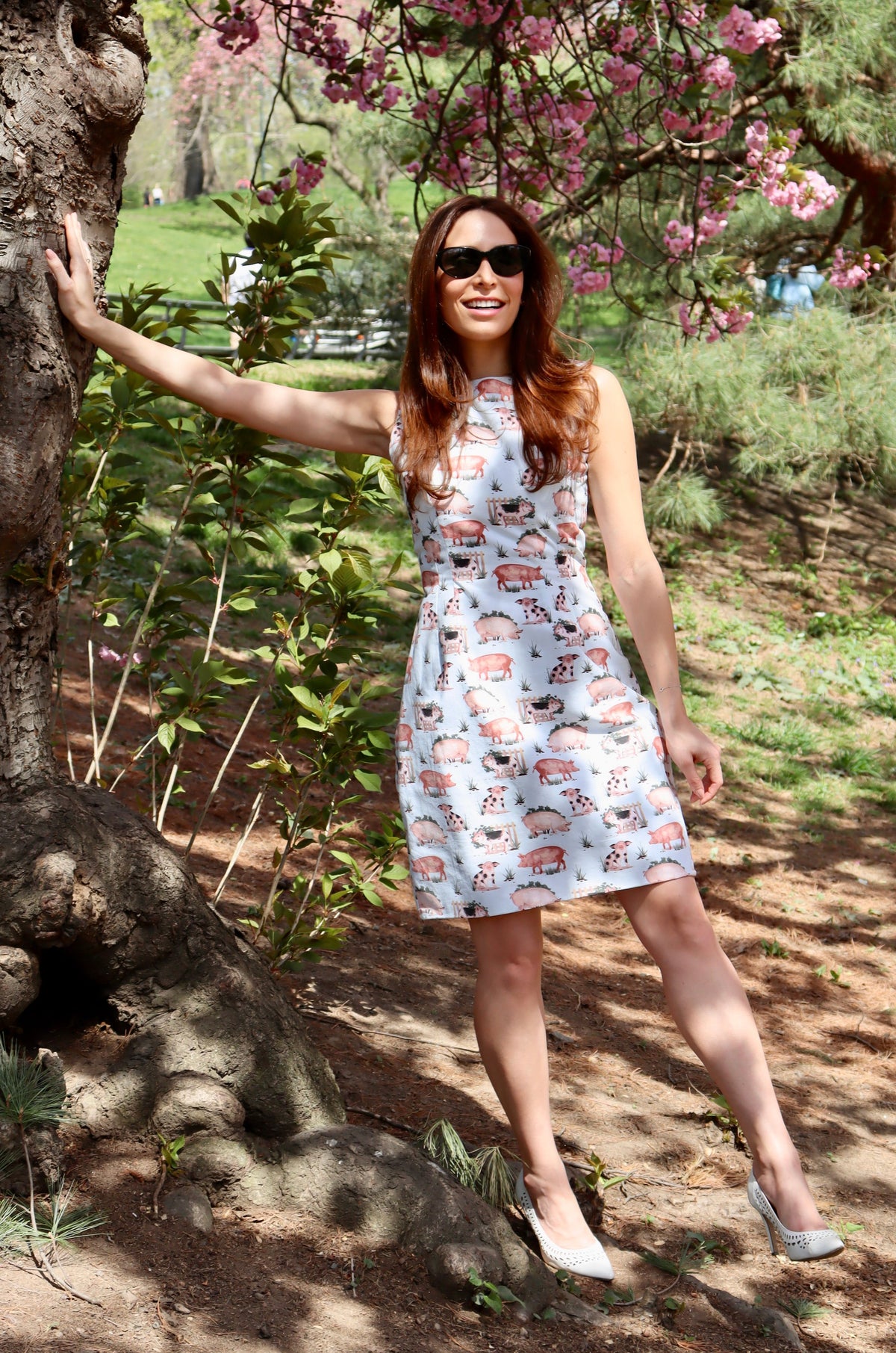 Model wearing short pig print dress leaning against a tree.