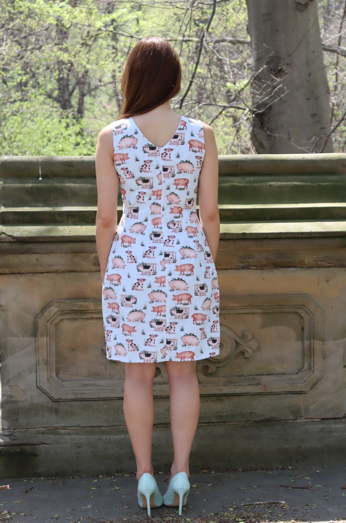 Back view of Model wearing short pig print dress leaning against a stone balustrade.