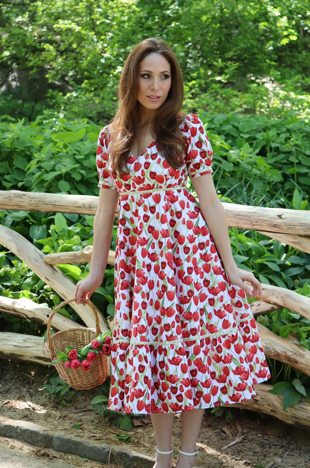 Model wearing midi length dress with a tulip print on white in front of a wood fence.