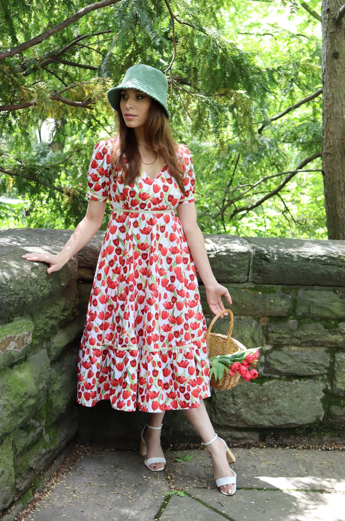 Model wearing midi length dress with a tulip print on white leaning against a stone wall.