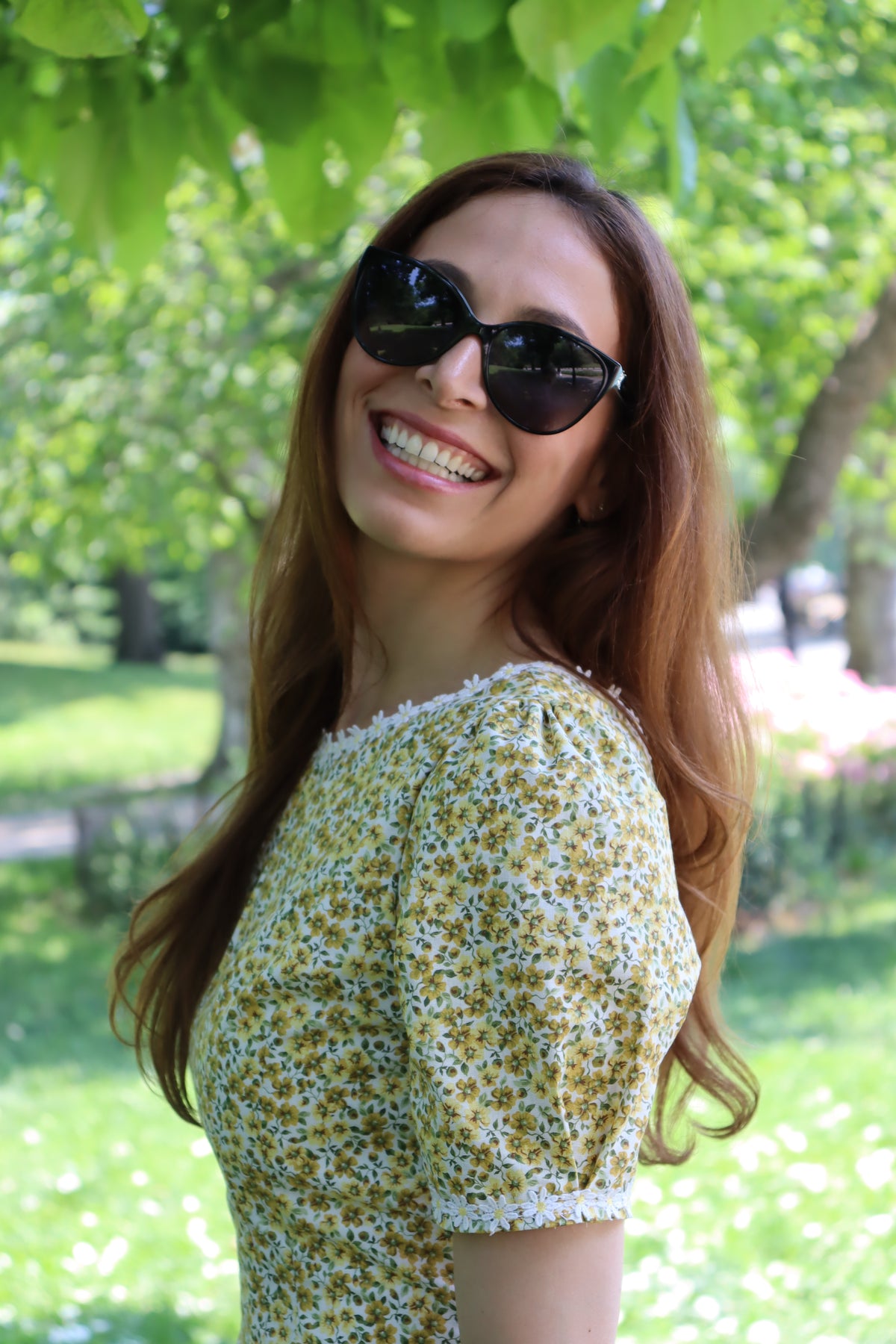 Photo of a model showing the detail of the sleeve of a short yellow floral dress with short sleeves and white daisy trim .