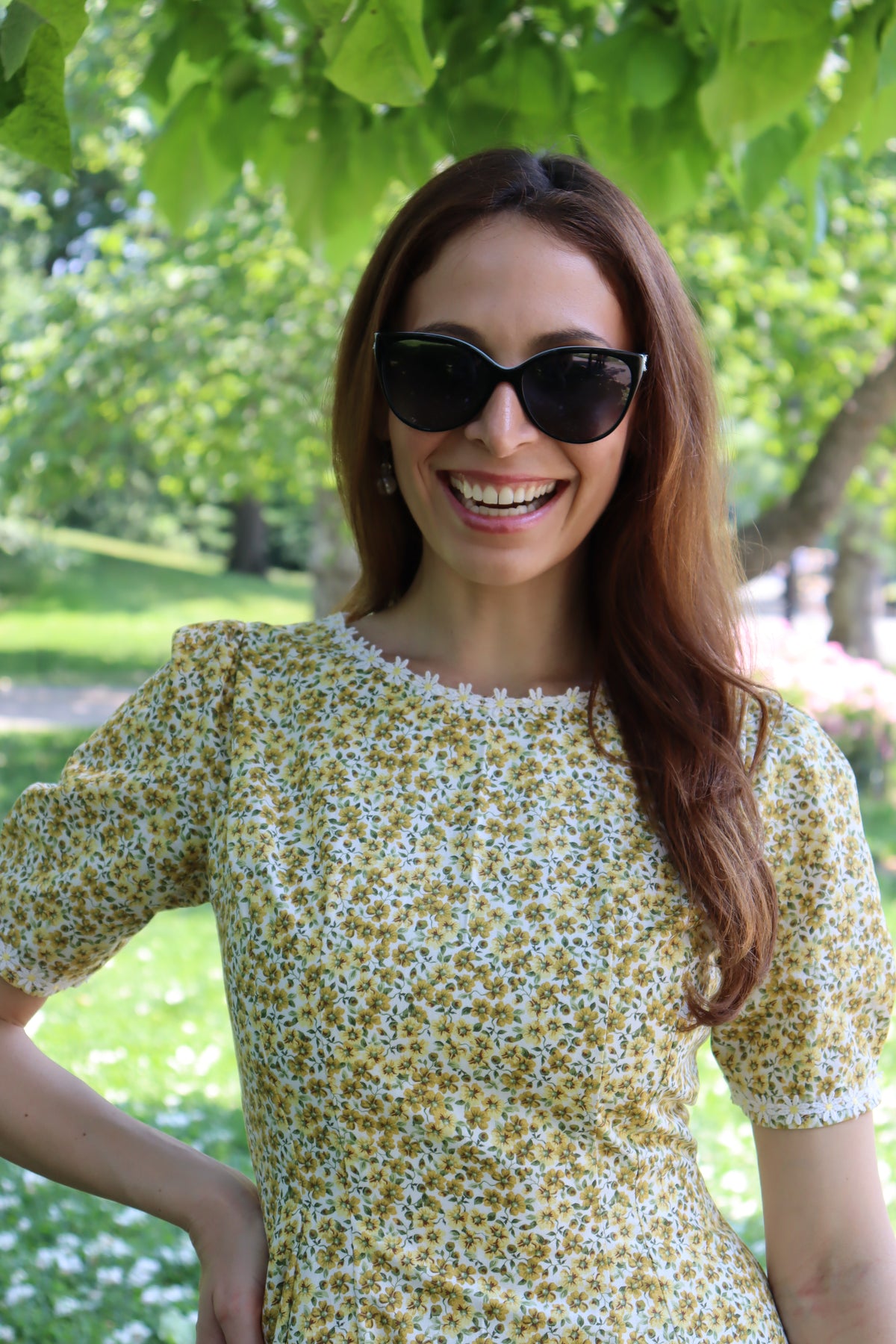 Photo of a model showing the detail of the front neckline of a short yellow floral dress with short sleeves and white daisy trim .