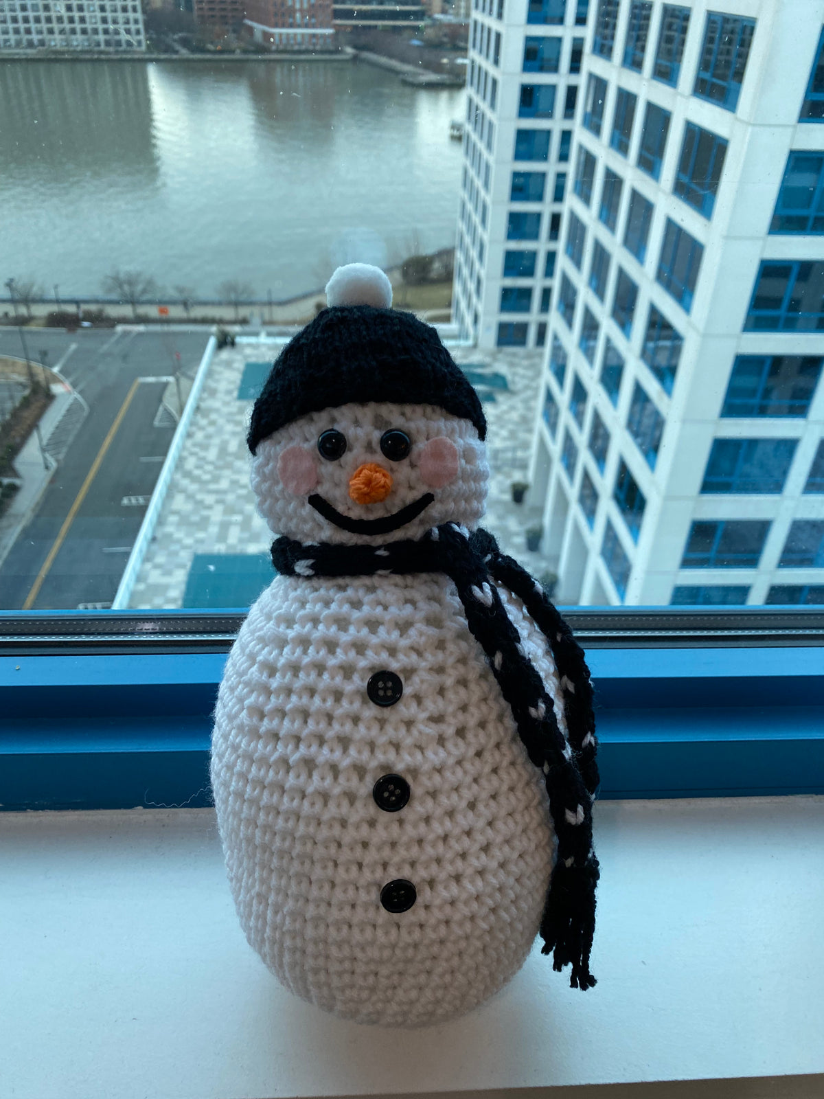 Cute crocheted snowman with black beanie and black scarf with hearts on it