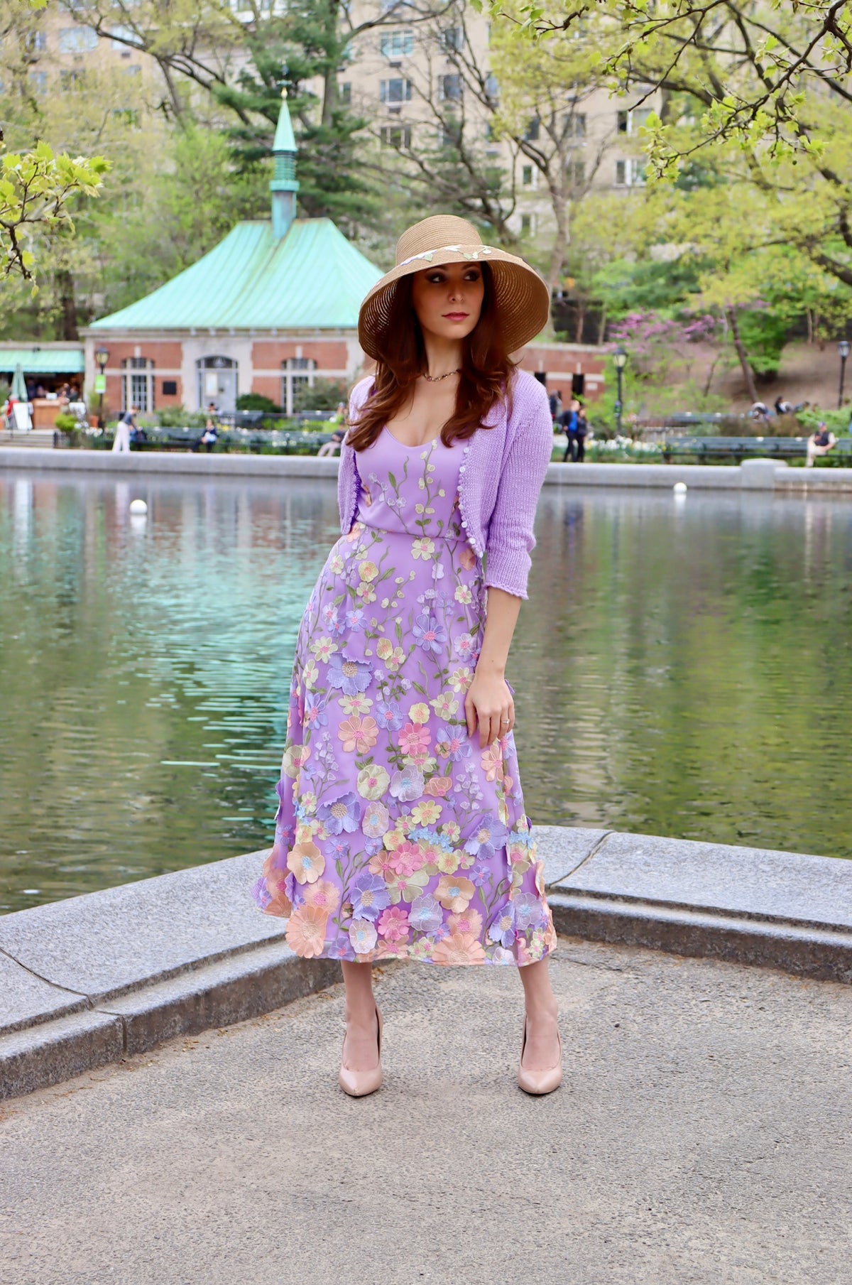 Model in lilac midi length dress with satin floral appliquéd details with matching lilac cropped sweater and floral detail straw sun hat.