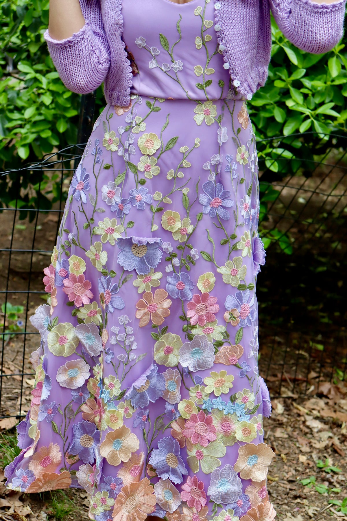 Up close and zoomed in image of lilac midi length satin floral appliquéd dress with blush pink and yellow flowers.