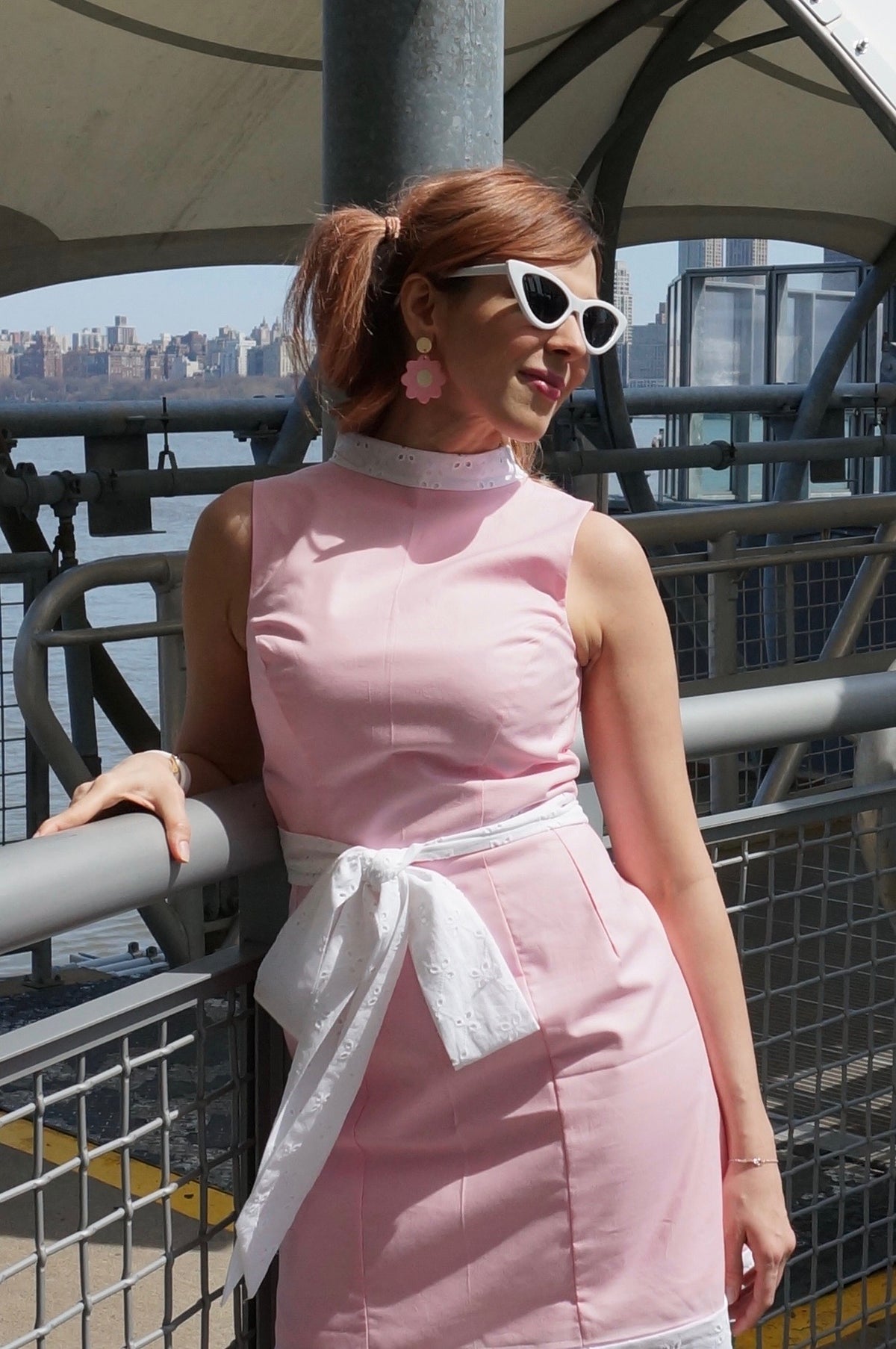 Model wearing a pink pure cotton with white eyelet trim and a big bow smiling looking off to the side.