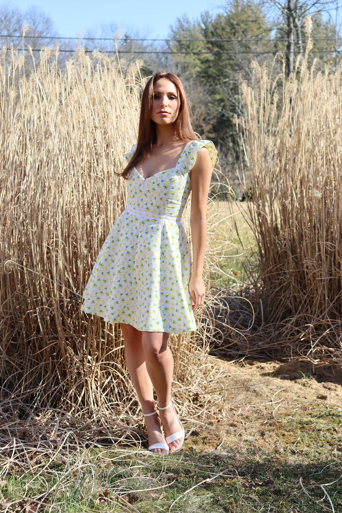 Model in lemon print dress in front of a field of hay.
