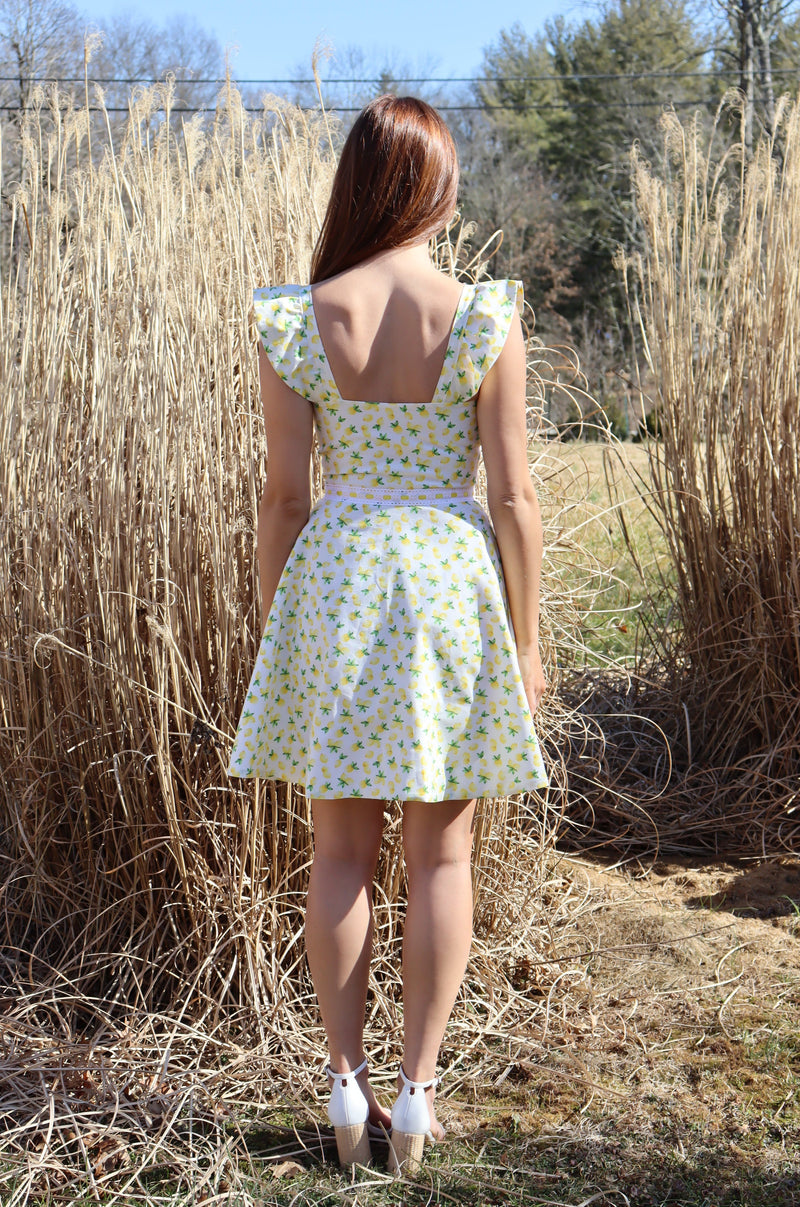 Back of model in lemon print dress in front of a field of hay.