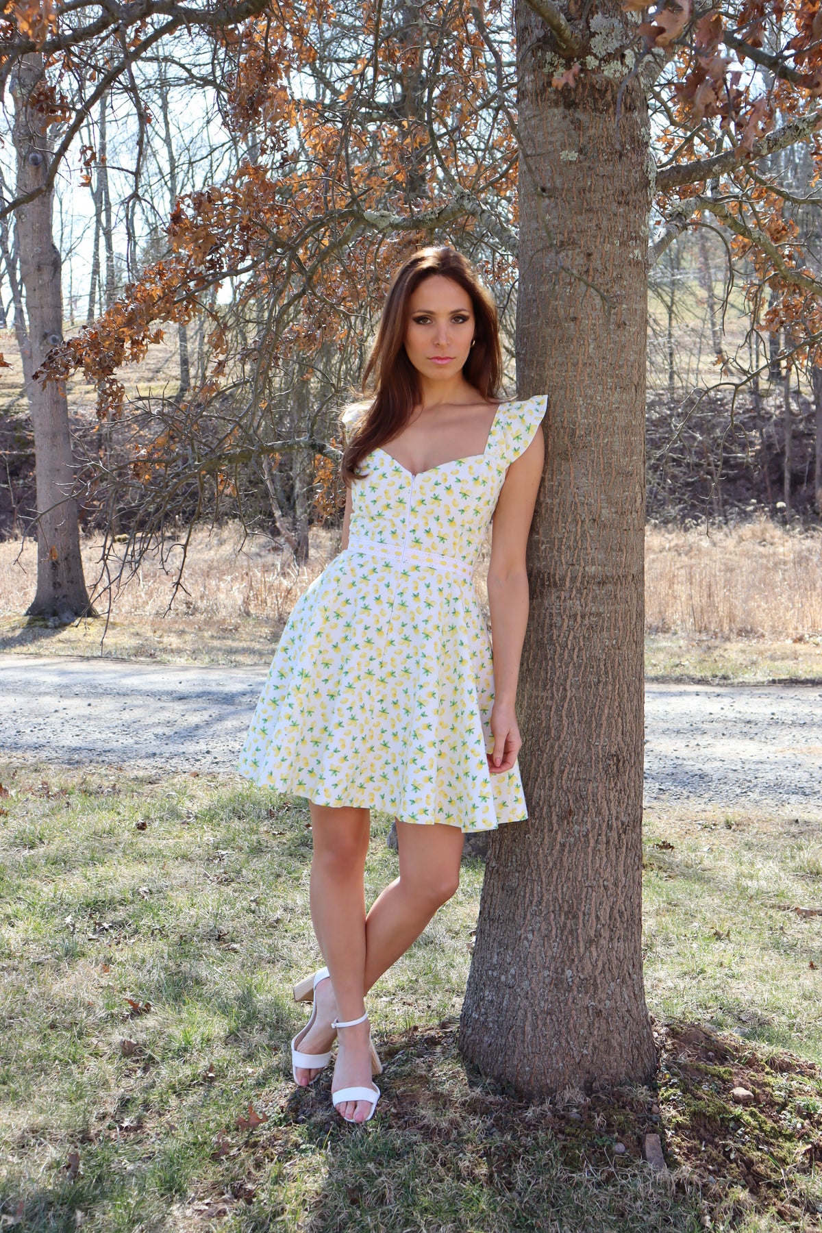 Model in lemon print dress posing next to a tree.
