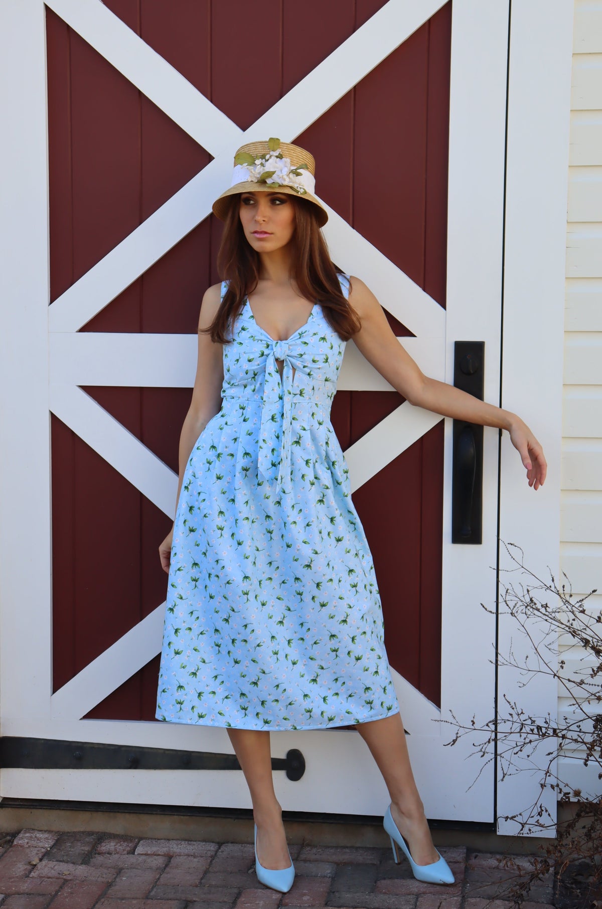 Model wearing a midi light blue dress with peek-a-boo bow front, in front of a barn.
