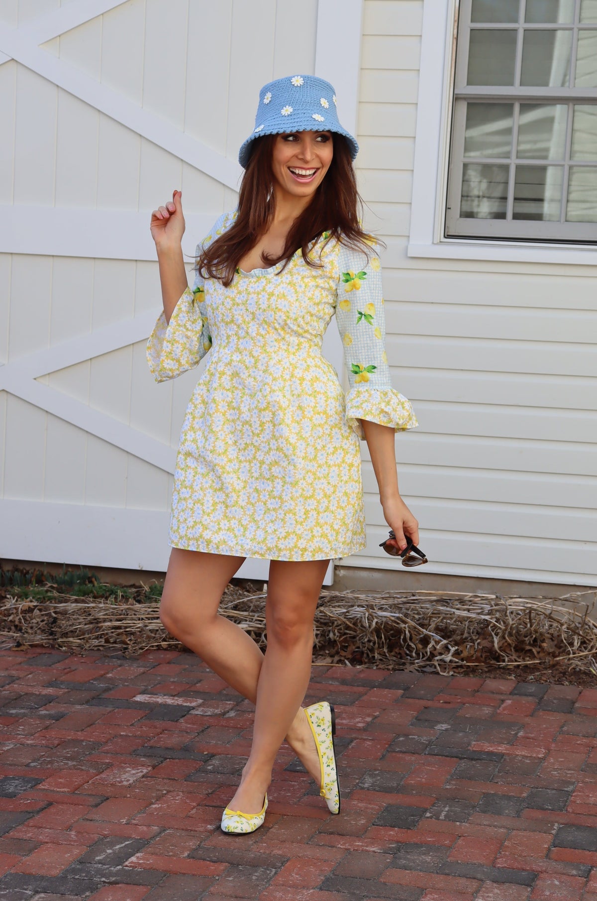Model in bucket hat with daisies wearing  Sweet Caroline Dress which combines a yellow daisy print with a light blue lemon print.