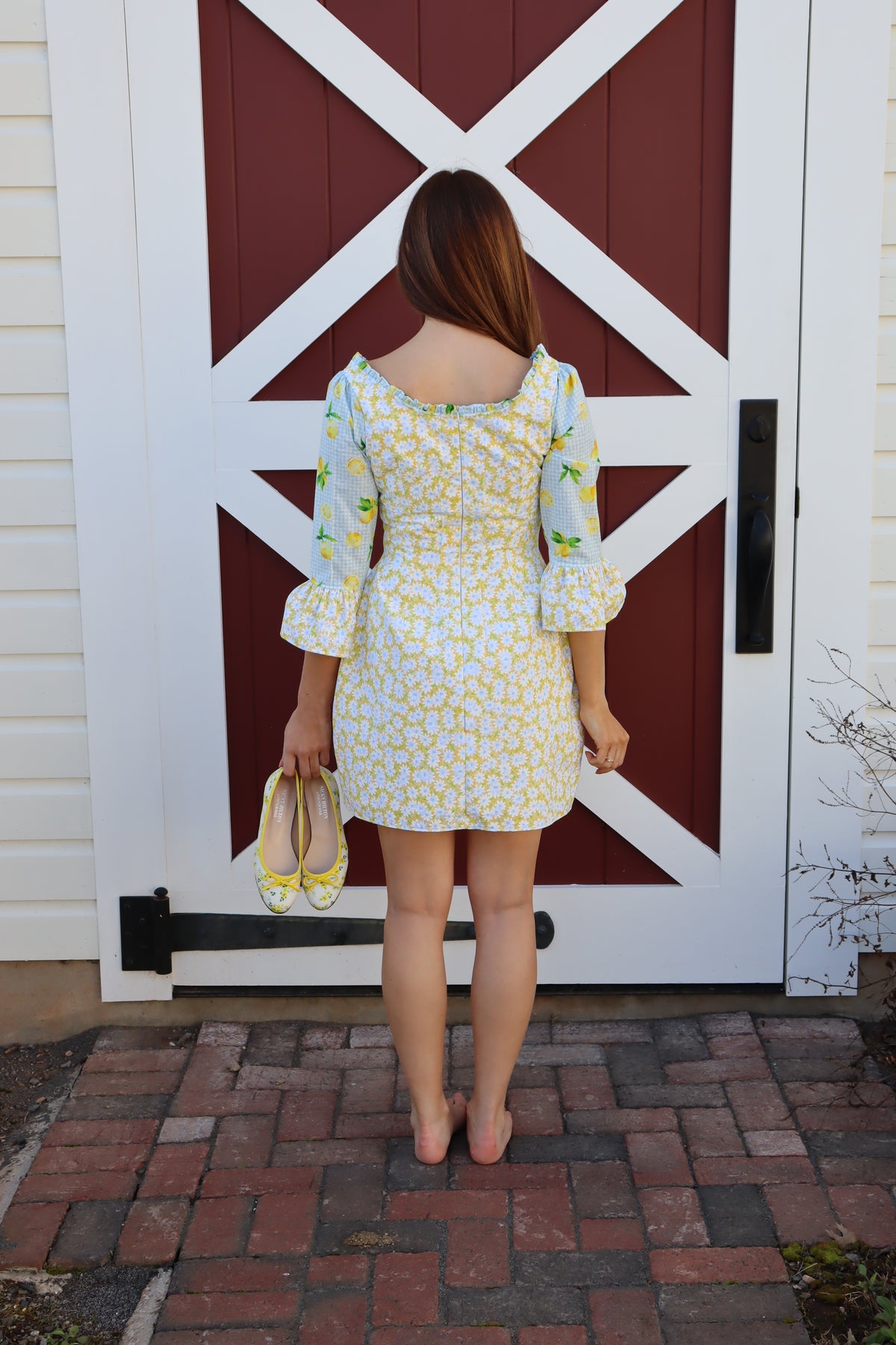 Back view of Model wearing  Sweet Caroline Dress which combines a yellow daisy print with a light blue lemon print.