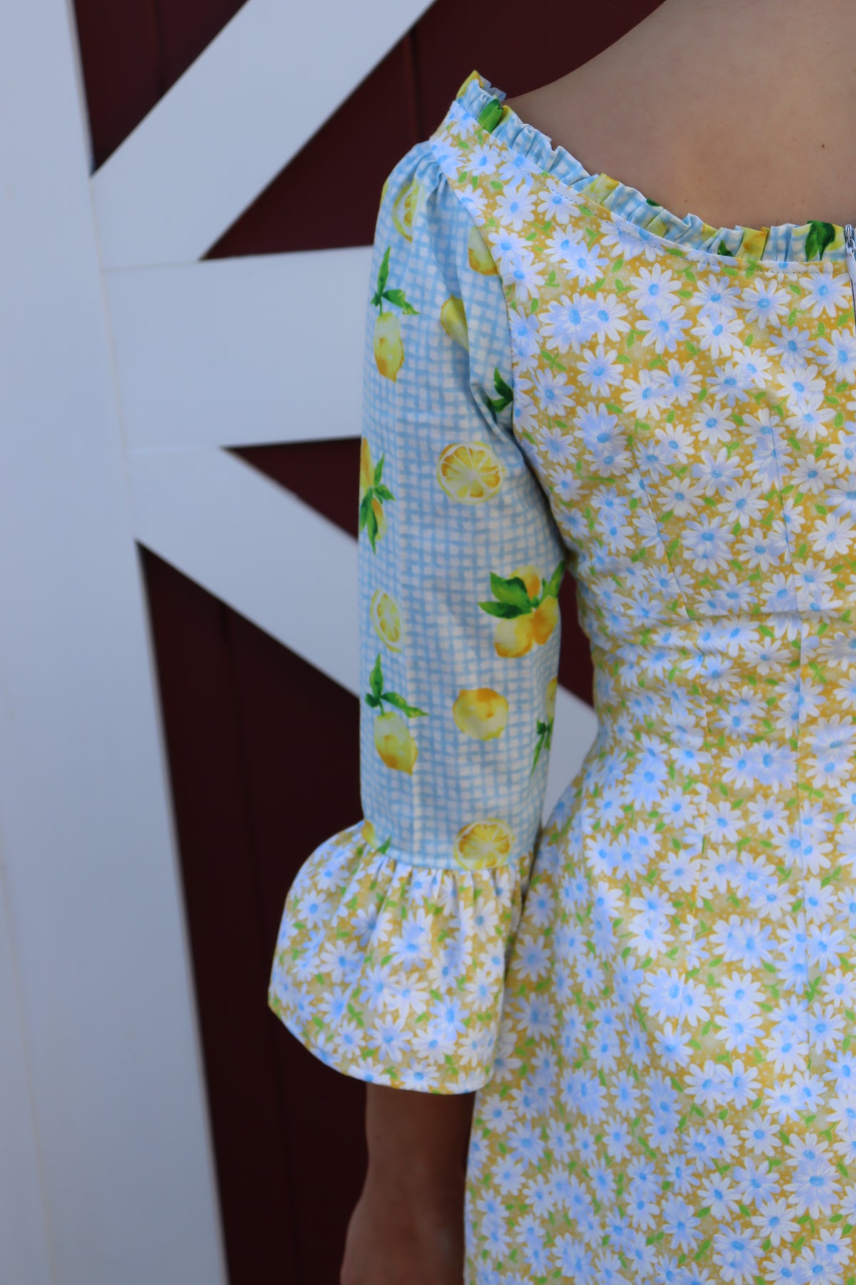 Close up of back of sleeve of Model wearing  Sweet Caroline Dress which combines a yellow daisy print with a light blue lemon print.