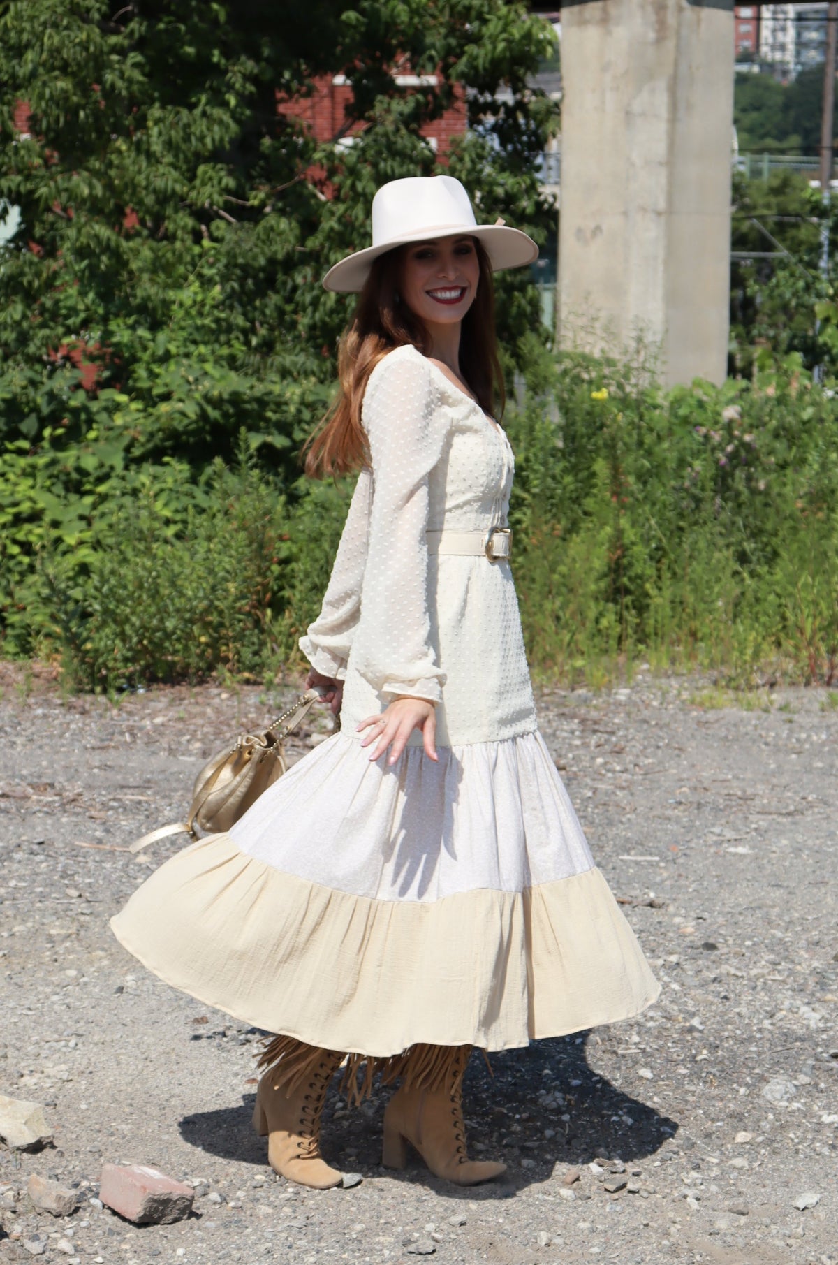 Model wearing dress with three different fabrics, Swiss Dot, Calico and Gauze midi dress, a belt, hat and purse smiling.