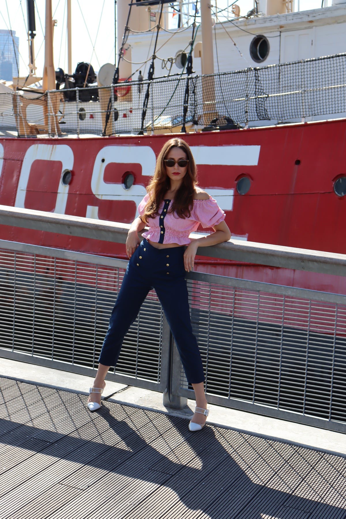 Model wearing jib top and navy cotton port capris leaning against a railing in front of a red boat.