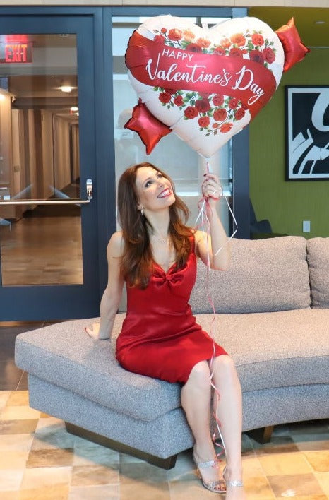 Model wearing red stretch taffeta dress sitting down holding a heart shaped balloon.