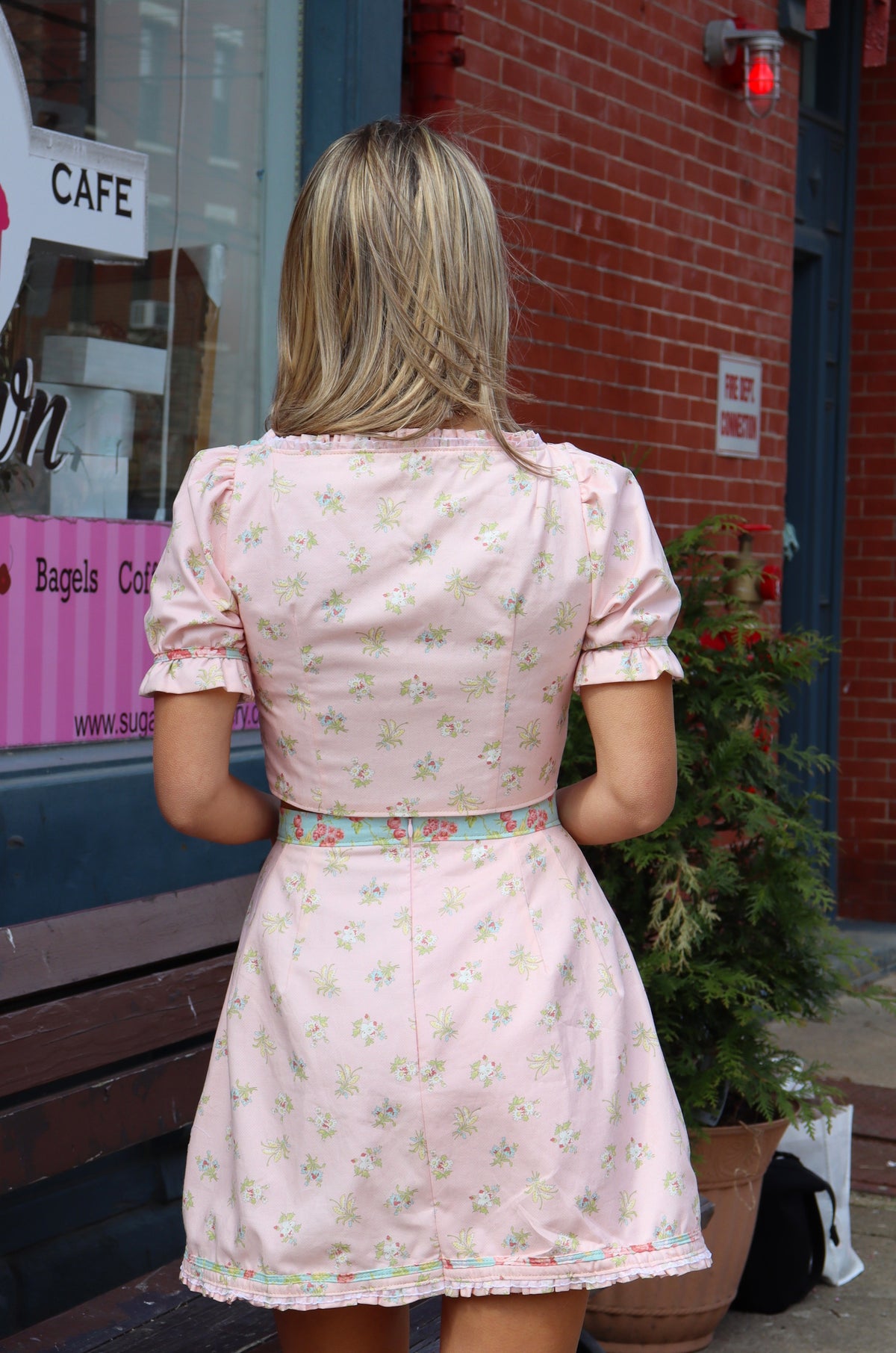 Back of model wearing a pink and aqua, 3/4 sleeve crop top with gold stitching and a pink and aqua skirt with gold top stitching.